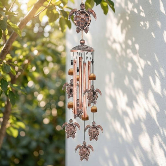 Decorative wind chime with turtle design hanging outdoors against a white wall.
