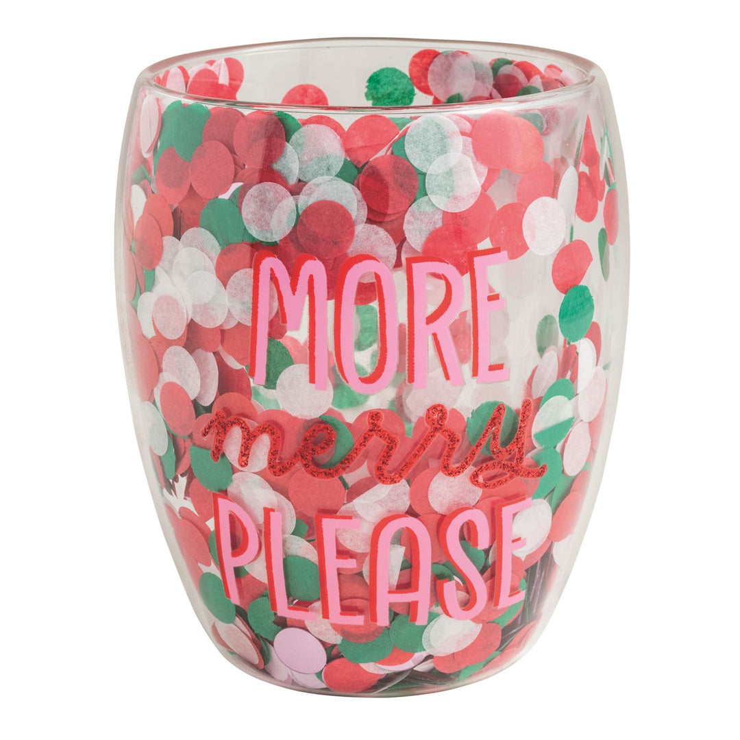 A clear double-walled stemless wine glass filled with red, green, and white round confetti, printed with the phrase More Merry Please in pink and red glitter lettering.