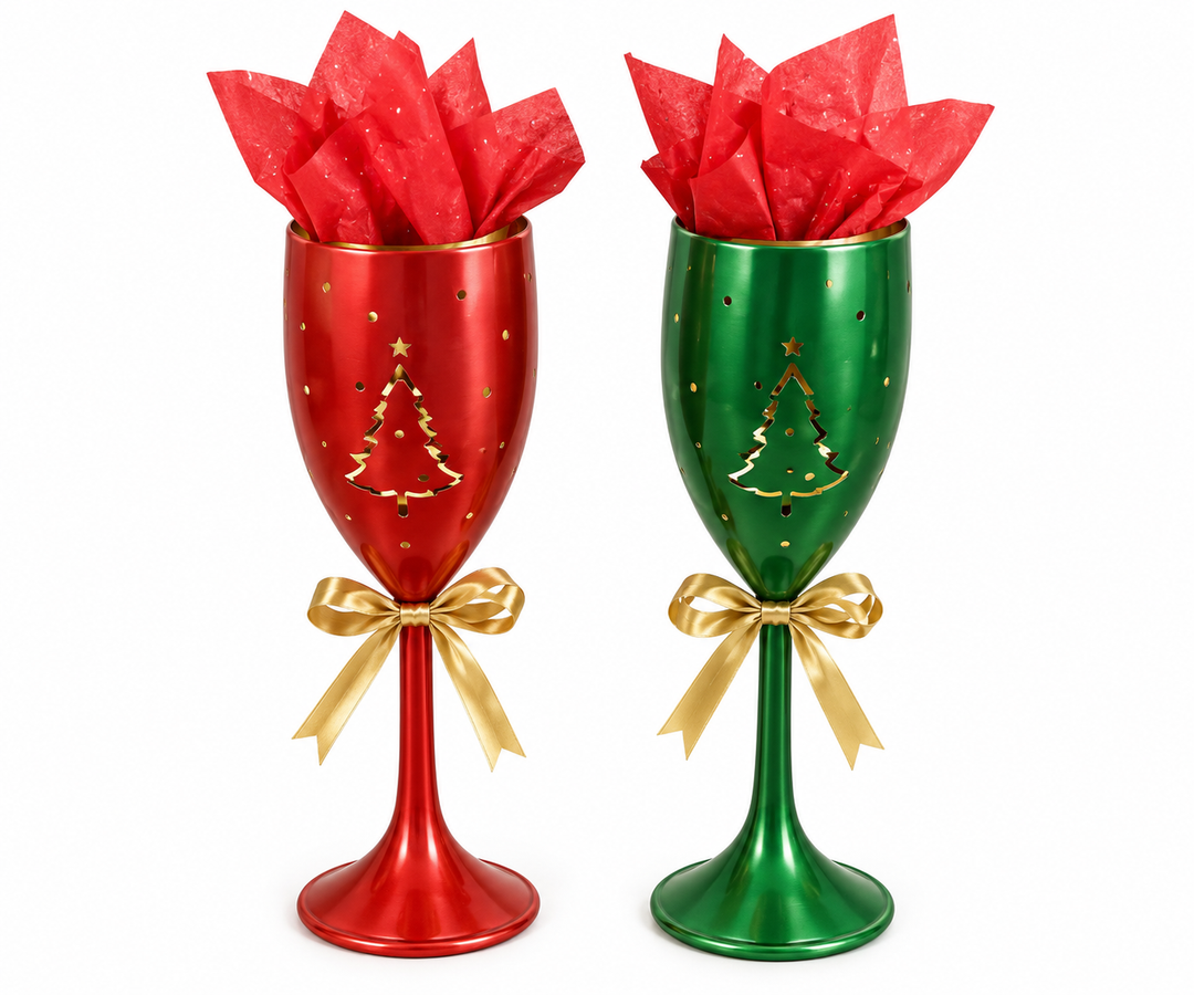 Two metal champagne-flute-shaped candle holders side by side — one red and one emerald green — each with a gold-tone cutout Christmas tree motif, scattered dot perforations, a gold satin bow at the stem, and red tissue paper arranged inside the opening.