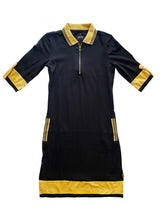 A knee-length black sheath dress with a quarter-zip polo collar, elbow-length sleeves, two front zip pockets, and gold contrast trim at the collar, cuffs, pockets, and hem.