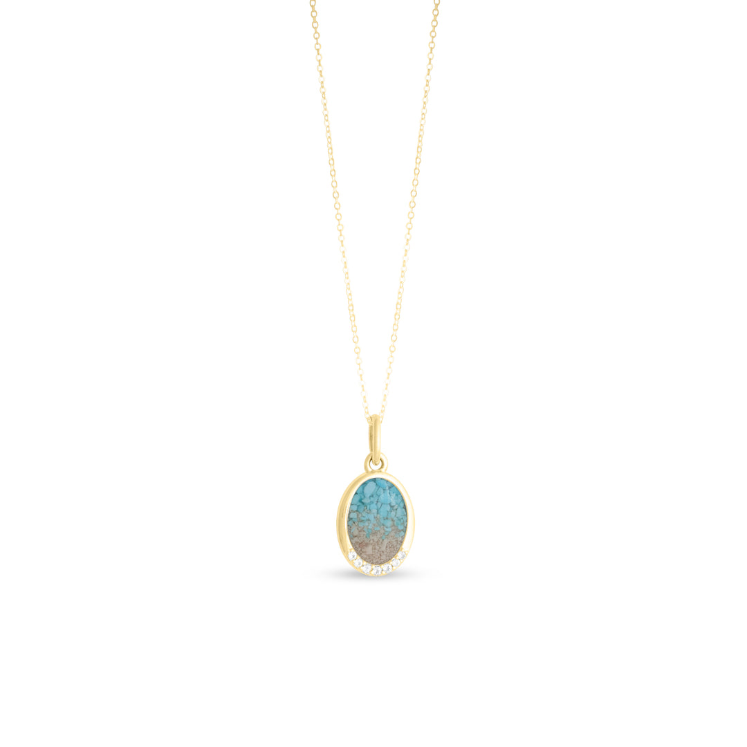An oval pendant necklace with a turquoise gradient stone showing natural matrix veining, set in a gold-tone bezel with small white topaz accents along the lower edge, hanging from a delicate gold cable chain against a white background.